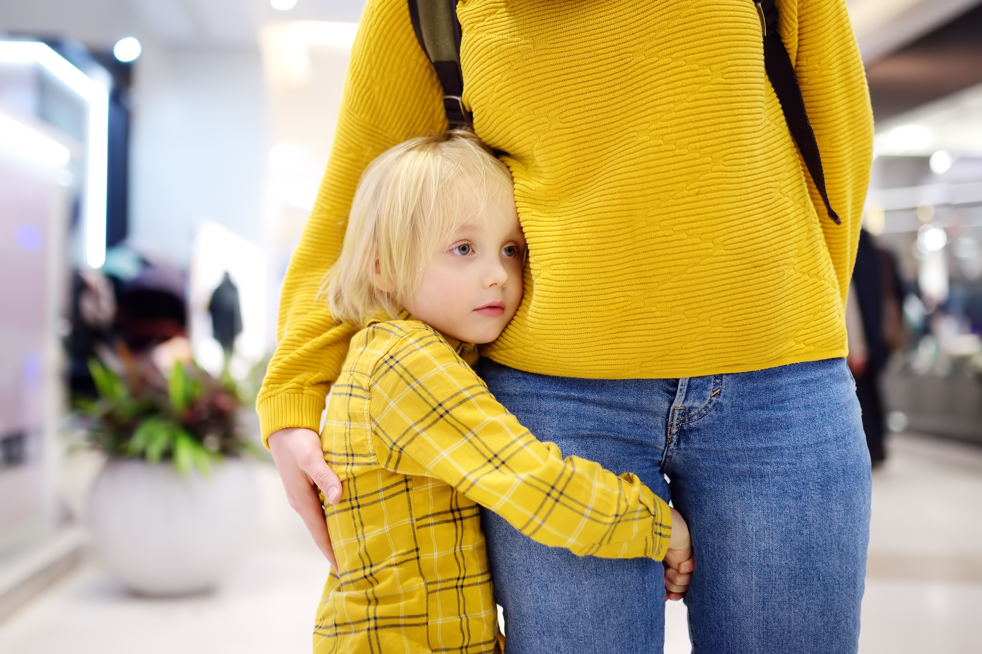 Child hugging his mother's leg, feeling anxious