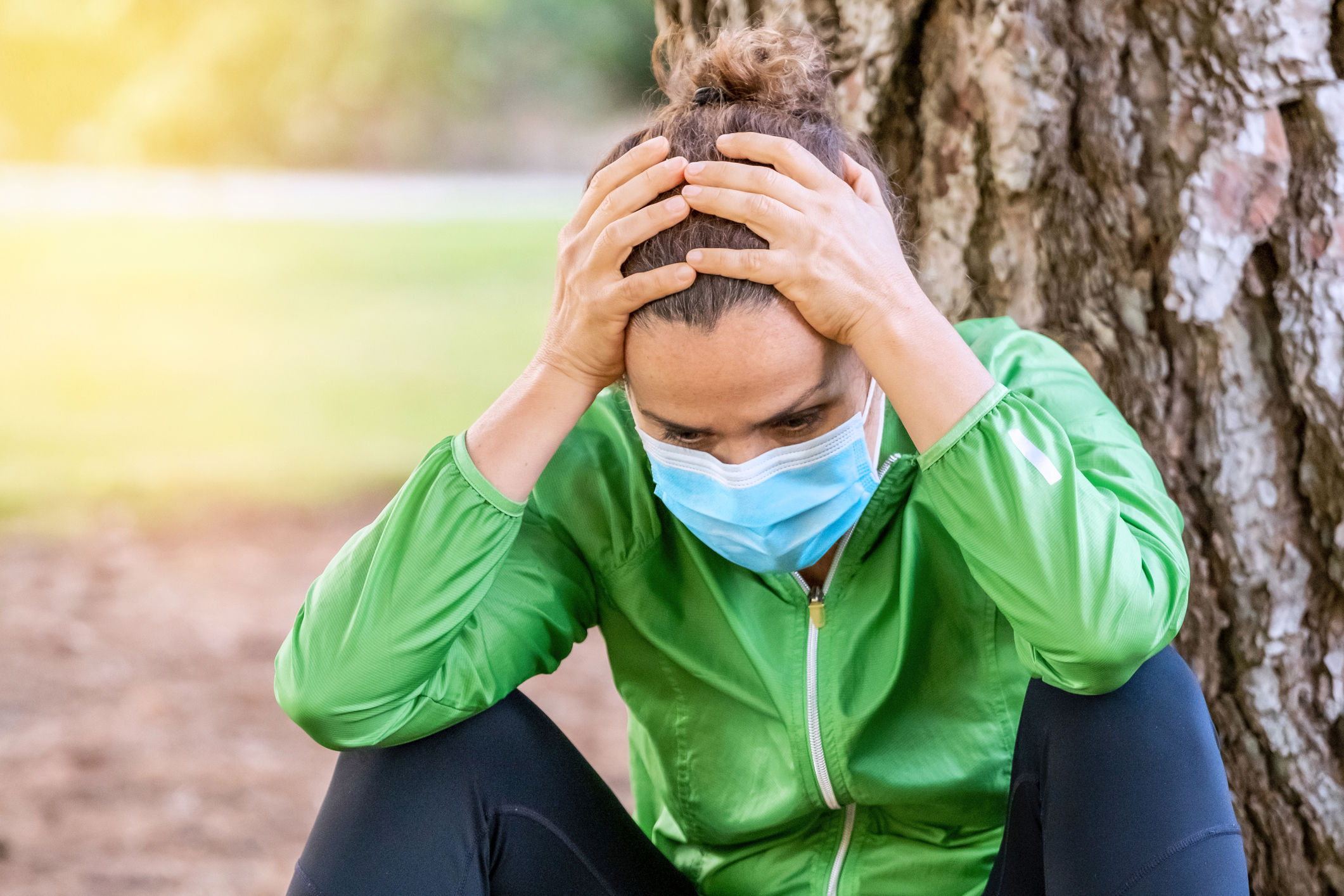 Woman with intrusive thoughts elbows on knees, with mask and green jacket