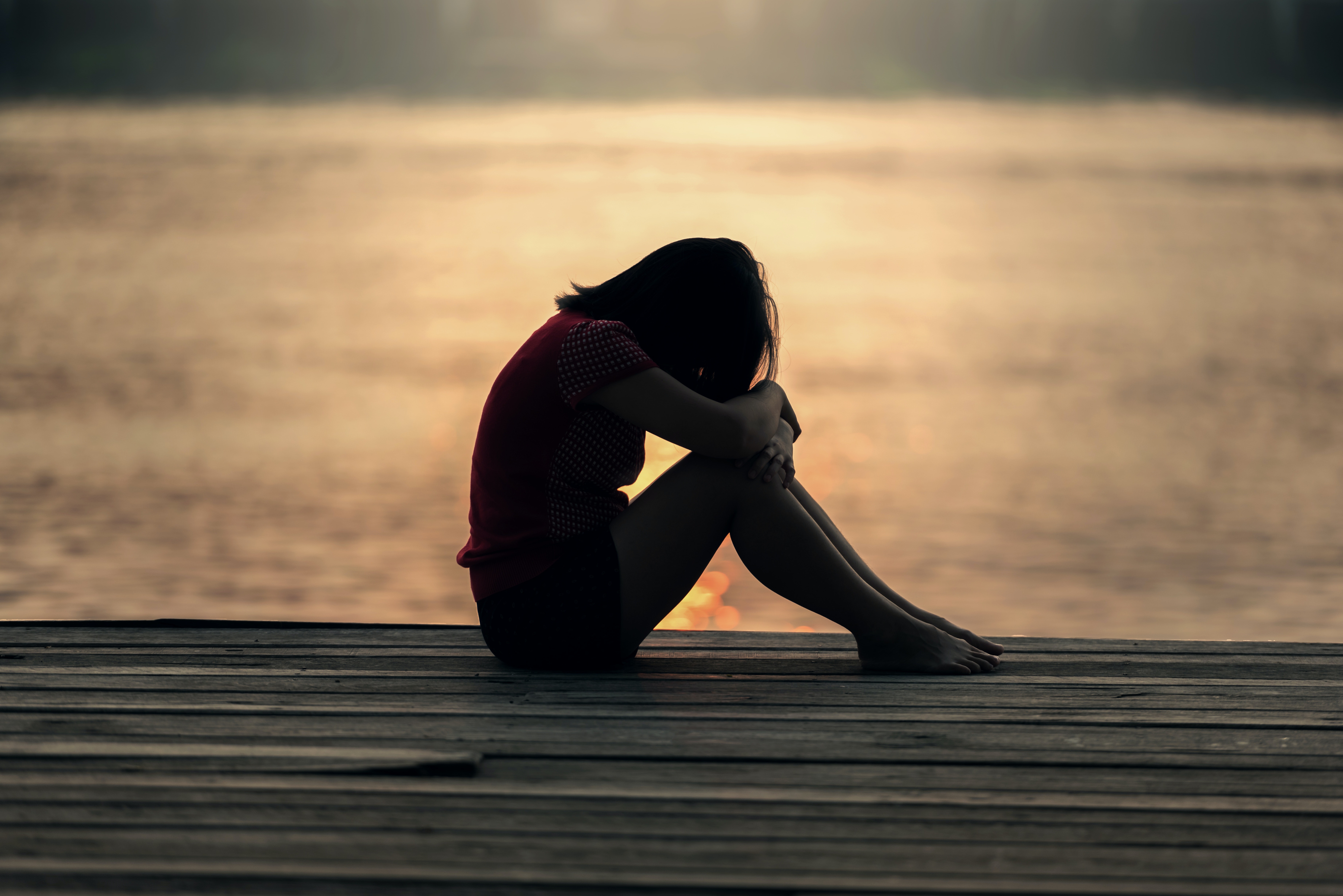 Depressed woman huddled on a dock overlooking water in St. Louis, MO
