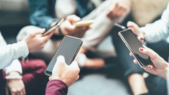 Teens use phones in a group. This relates to concepts of teen therapy in Kansas City, MO.