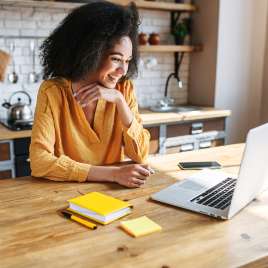 A woman smiles while using a computer. This relates to online therapy in Missouri. 