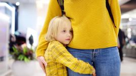 Child hugging his mother's leg, feeling anxious