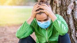 Woman with intrusive thoughts elbows on knees, with mask and green jacket
