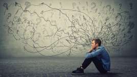 Man sitting on floor with knees up. Black sketches of anxiety are coming out of his head making a cloud