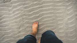 Barefoot man walking on sand.