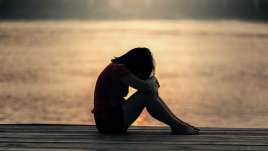 Depressed woman huddled on a dock overlooking water in St. Louis, MO